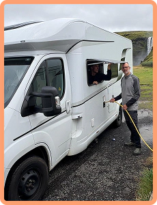 Cliente che collega il cavo di alimentazione a un camper con una cascata islandese sullo sfondo